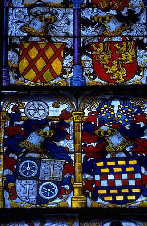 Light illuminates brightly colored coats of arms depicted in stained glass. Cologne, Germany. 13th 