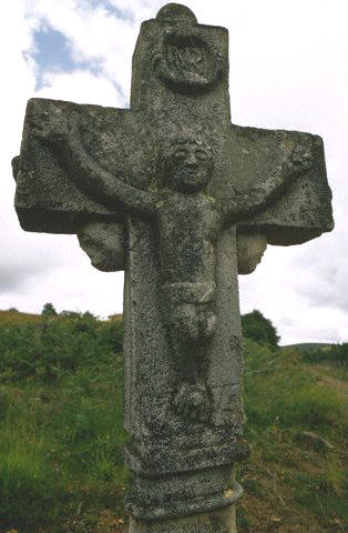 A stone cross, bearing an image of crucifixion, stands beside a route formerly used by pilgrims